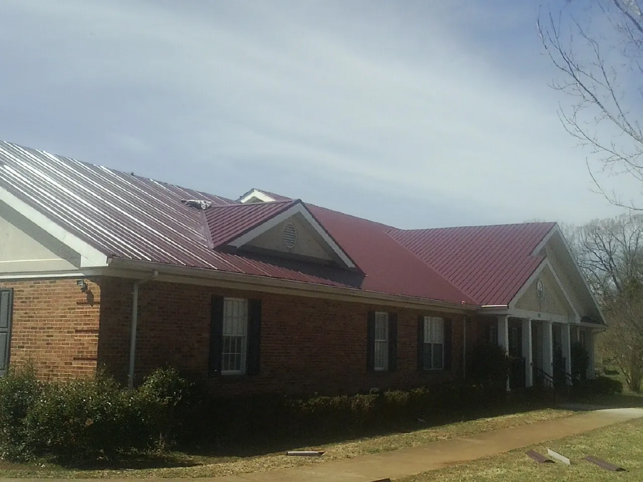 Red metal roof with gabled entries on a long brick building, from a Hail Damage Roof Repair job in San Pablo