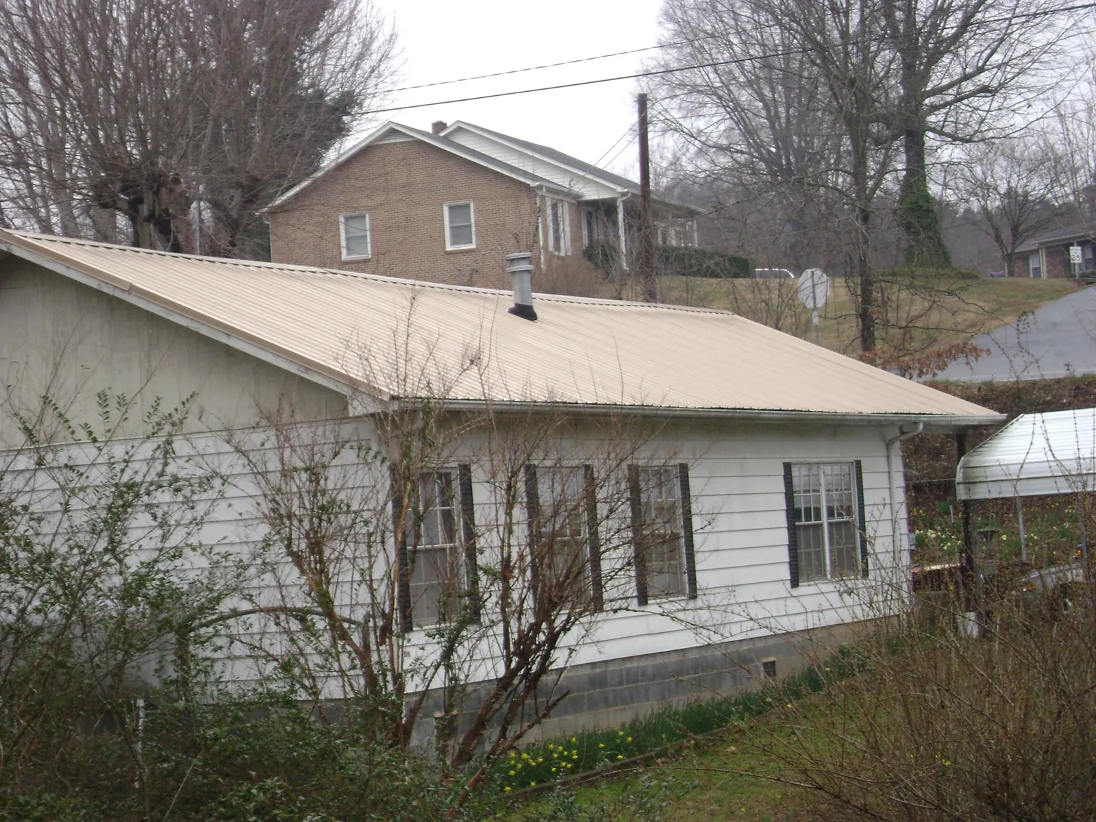 Tan metal roof on a white sided house set into a hillside — Commercial Roofing by Roofing Brothers in San Pablo